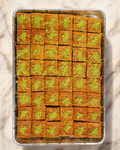 Baklava with green pistachio filling in a metal tray on a marble surface