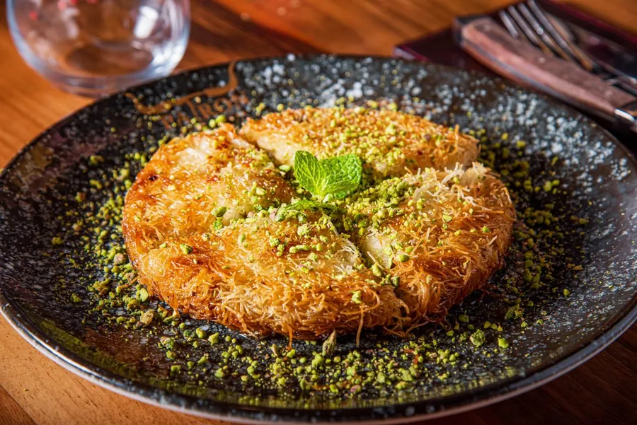 Kunafa garnished with crushed pistachios on a decorative plate